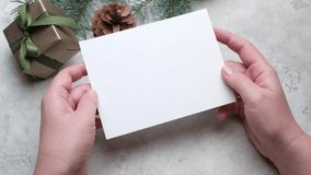 Hands present a blank greeting card mockup alongside beautifully wrapped gift boxes and pinecones, creating a warm holiday atmosphere, camera pans across the scene - Powered by Shutterstock - Get 15% off with code: PIKWIZARD15