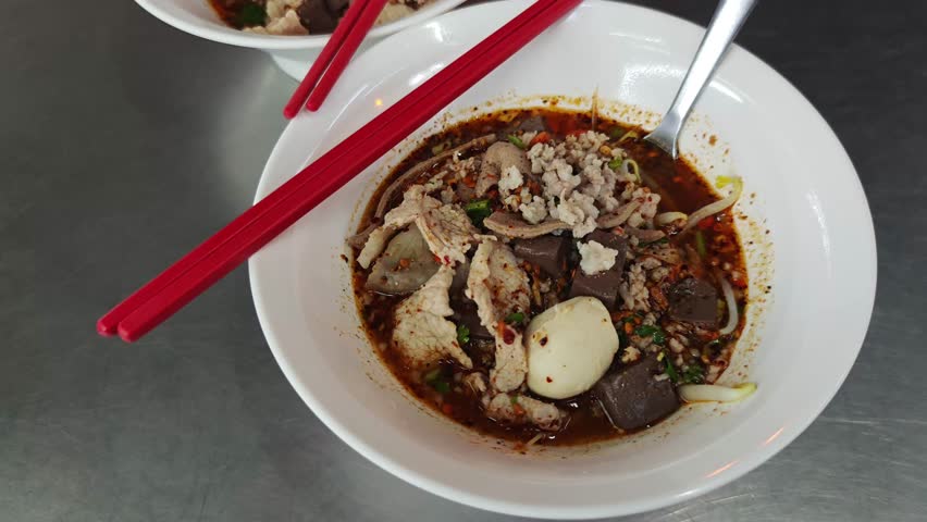 A delicious bowl of spicy noodle soup featuring a mix of tender meats, vegetables, and flavorful broth.