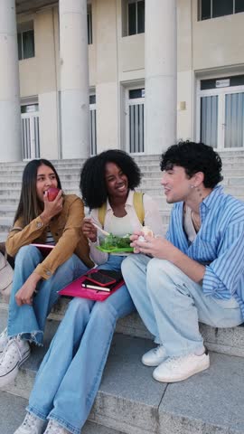 Group of multiethnic university students eating and talking during their break on the campus stairs