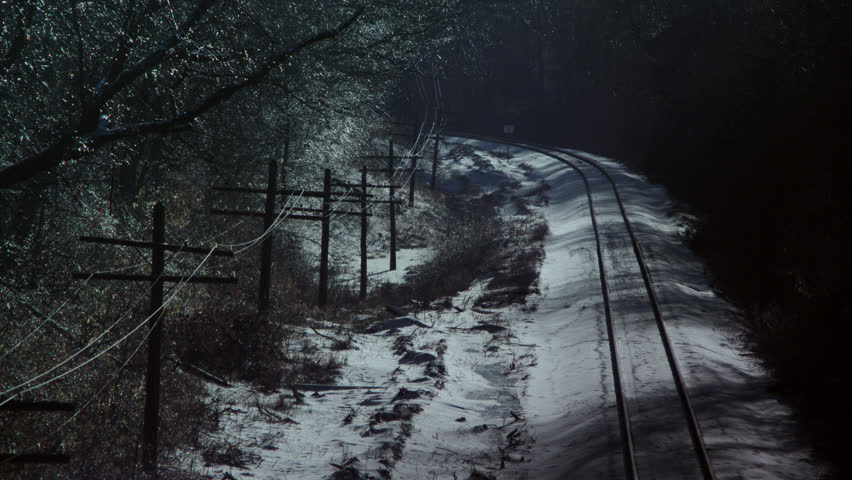 Shadows cast by barren trees crawl over ice and snow-covered railroad tracks in a woodlands wonderland after an ice storm.
