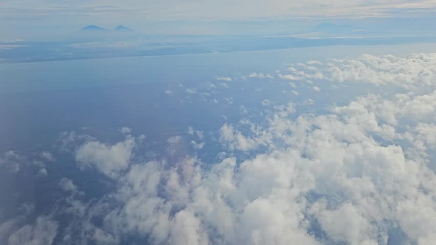 Vast aerial landscape of thick white clouds transitioning to the ocean and distant mountains under a bright sky