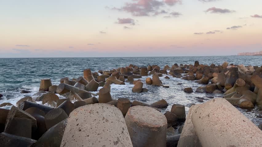 Waves crash against concrete breakwaters on the Alexandria coast at golden hour, capturing coastal beauty while reflecting rising sea levels and the growing impact of climate change.