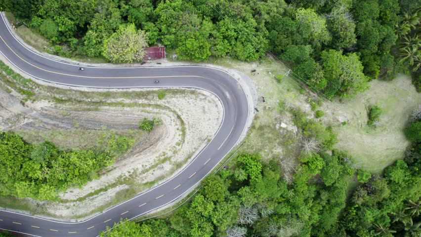 Aerial view of an asphalt S-curve road snaking through a lush green tropical forest and hills. Beautiful nature landscape travel