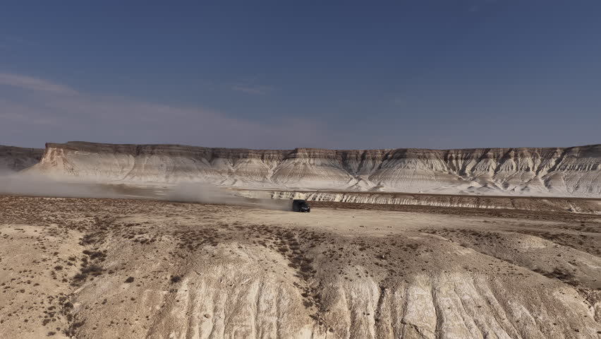 Aerial shot of an suv driving through a dusty desert canyon of Bozjyra or Bozzhyra