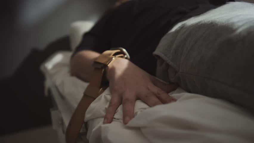 Selective-focus of a patient with a mental disorder with arms tied to a hospital bed, highlighting psychiatric care, safety measures, and medical context in 4K.