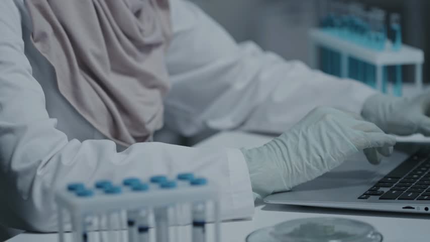 Slow-motion of a lab technician in gloves typing on a portable computer, highlighting lab work, research, and technology in a controlled environment.
