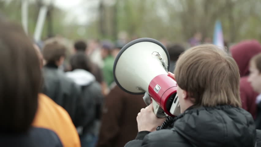 Portrait of a young man shouting with a megaphone at a crowded place