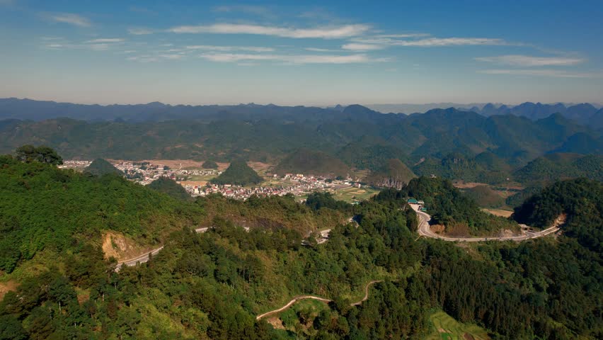 Cinematic aerial sweep over winding roads on the mountainsides of Northeast Vietnam, revealing the residential plains and valley below the majestic mountain range.