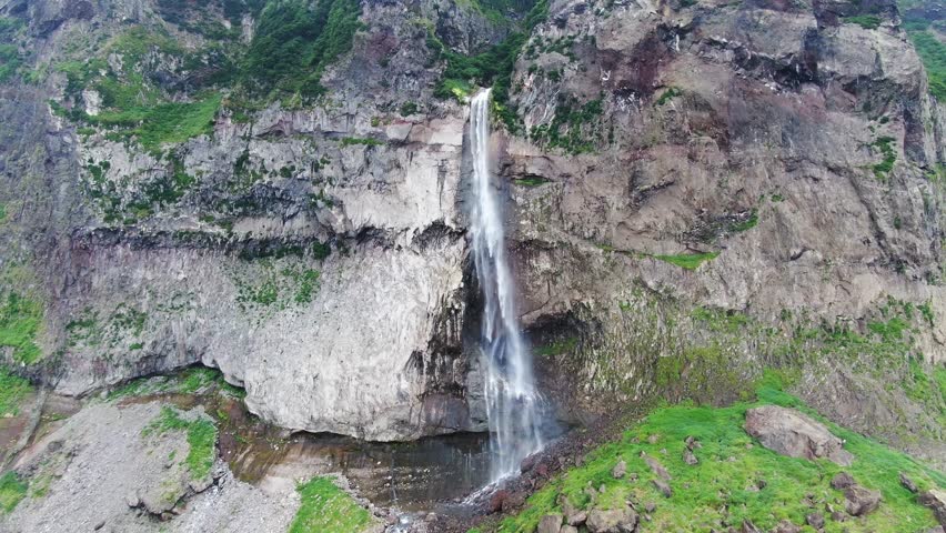 A cinematic aerial shot of a dramatic waterfall on a sea cliff in the Pacific Ocean. Kuril Islands.