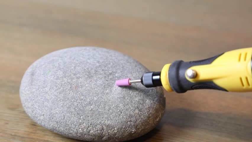 Rotary tool with a grinding bit creating a small hole on a gray stone. Crafting and engraving on rock material.