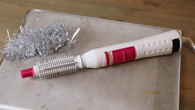 Electric hair curler and brush with silver tinsel resting on a metal tray, hair styling tool for beauty and personal care. - Powered by Shutterstock - Get 15% off with code: PIKWIZARD15