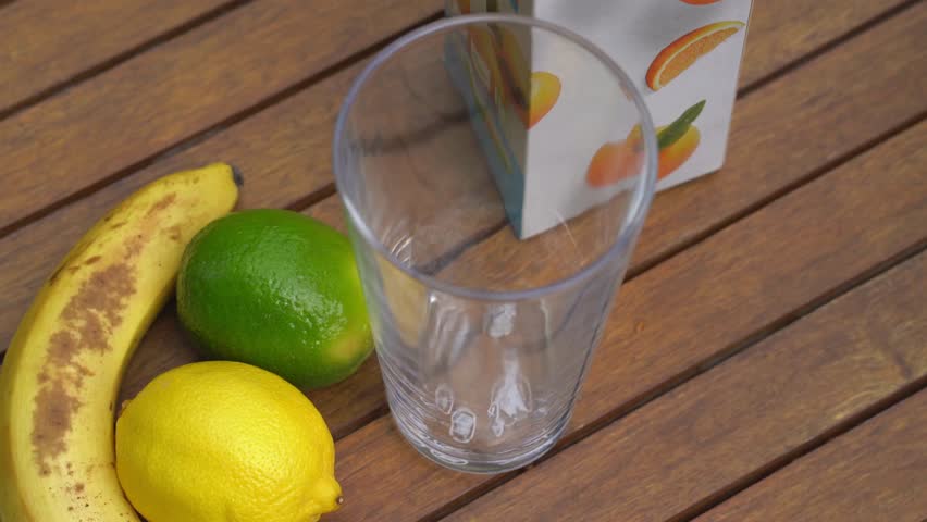 A clean tabletop scene with fresh fruits (lemon, banana, lime) next to a glass and a hand pouring juice, ideal for beverage concepts, juice-making intros, kitchen lifestyle, and health-focused videos.
