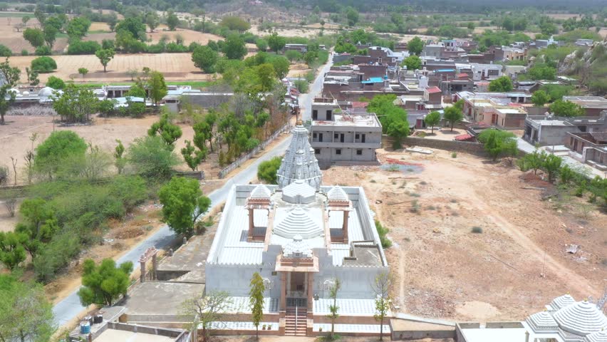 White temple with domes and spires at edge of rural village, surrounded by dry fields and rocky hills.