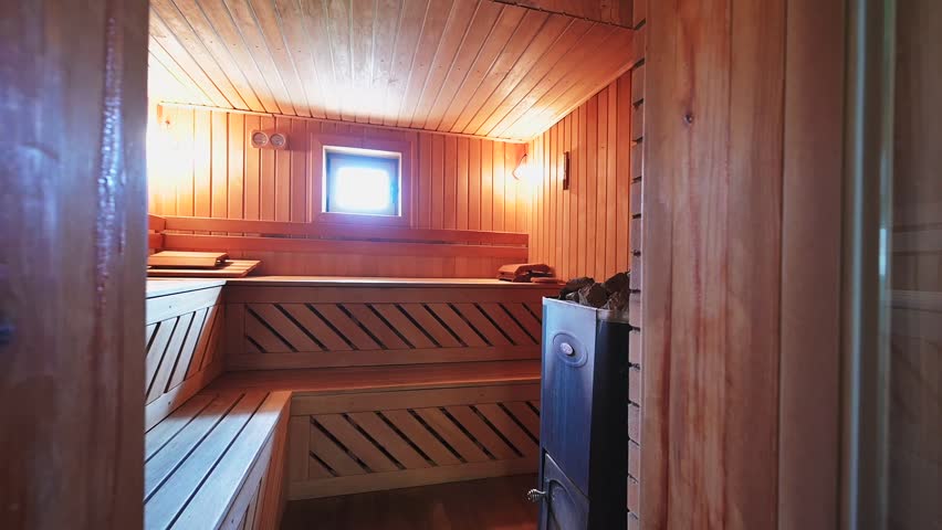 Cozy wooden sauna with tiered benches, warm lighting, and a heater. A small window lets in natural light, creating a serene, relaxing atmosphere