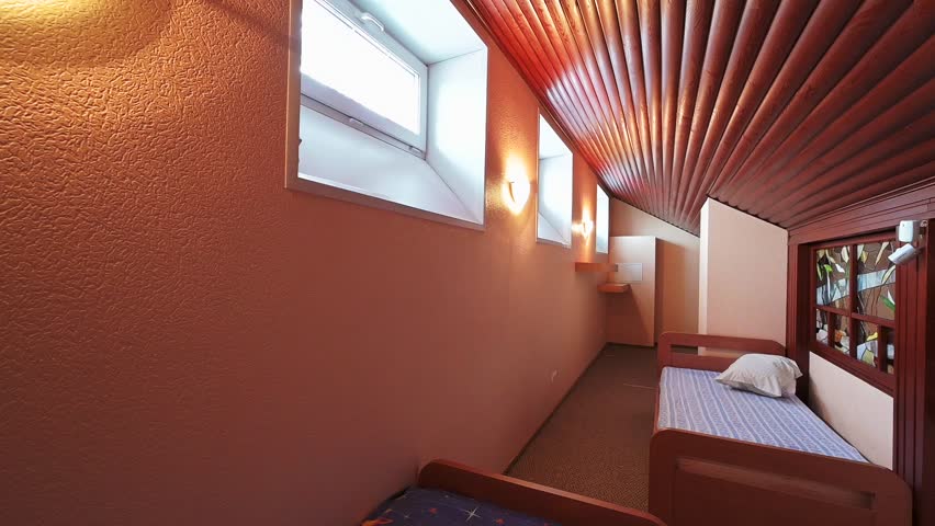 Compact bedroom with two single beds, a unique slatted wooden ceiling, and stained-glass windows. Warm lighting creates a cozy, intimate atmosphere