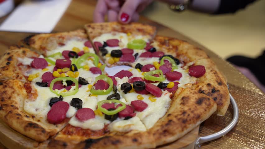 Close up view of a hand taking a cheesy slice of pizza with pepperoni and vegetables.