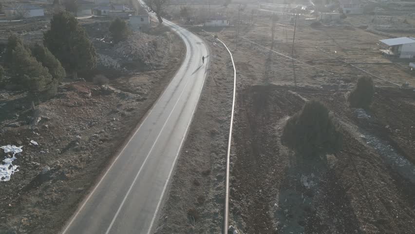 two cyclists are riding along an empty paved road, flooded with sunlight, in the mountains on a winter day