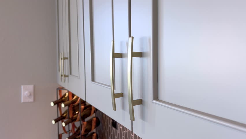 A detailed close-up of modern gold pulls on light gray kitchen cabinets. The cabinet surface is clean and reflects soft indoor lighting.