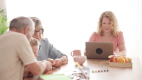 Focused woman working remotely on her laptop at a dining table while her child and grandparents are playing and drawing in the background - Powered by Shutterstock - Get 15% off with code: PIKWIZARD15