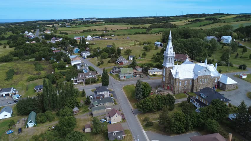 Aerial view of a road intersection in the village of Saint-Octave-de-Métis, where two cars are traveling near its church, overlooking the rural and agricultural landscape. Quebec, Canada, 2025.