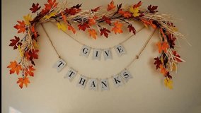 Rustic Give Thanks banner hanging on a beige wall surrounded by colorful artificial autumn leaf garland and foliage decoration for Thanksgiving holiday season - Powered by Shutterstock - Get 15% off with code: PIKWIZARD15