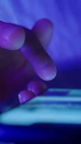 Close-up of hands holding a phone and scrolls social media feed at night. Concept of digital life, constant online interaction or technology overuse. Vertical video