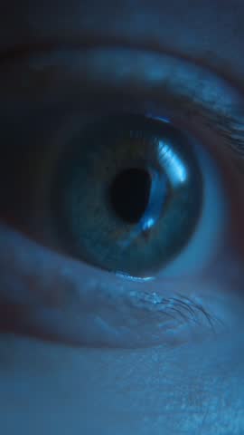 Macro view of a nervous human eye looking at display, illuminated by blue smartphone screen light, representing anxiety, social media addiction, and late-night doom scrolling. Vertical video