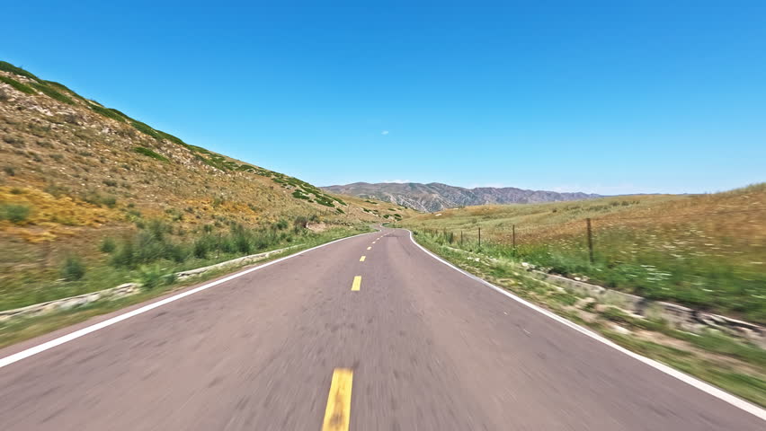 Asphalt road winding through dry hills landscape under blue sky
