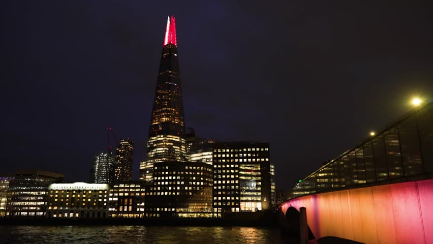 Night view of The Shard in London, framed by modern architecture and lights, with illuminated facade against dark sky for dramatic skyline.