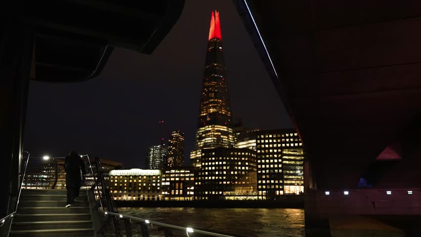Night view of The Shard in London, framed by modern architecture and lights, with illuminated facade against dark sky for dramatic skyline.