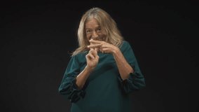 Senior blonde woman smiling and stretching clasping hands forward in studio wearing teal dress; playful joy. - Powered by Shutterstock - Get 15% off with code: PIKWIZARD15