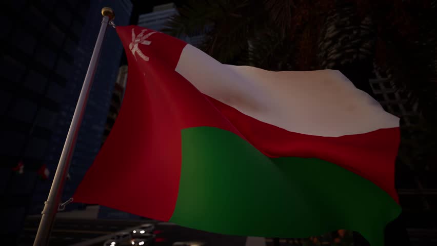 Oman national flag waving at night in a modern city illuminated by street lights, buildings and moving traffic within an urban skyline. The dark sky contrasts sharply with the vibrant colors of the standard, which is spotlighted from below, making the red, white, and green sections clearly visible against the void. In the background, the majestic domes and minarets of the Sultan Qaboos Grand Mosque or the Royal Opera House glow with architectural lighting, providing a culturally rich context. The bokeh effect of passing cars creates a stream of red and white orbs, signifying the constant motion of the metropolis. The fabric ripples gently in the cooler evening air, creating a hypnotic rhythm. This scene encapsulates the nightlife and sophisticated infrastructure of the country. It serves as a perfect visual for news segments wrapping up daily events, documentaries about Islamic culture in the modern age, or travelogues showcasing the safety and beauty of Arabian cities after dark. The vertical red stripe at the hoist anchors the visual, while the emblem reflects the heritage amidst the electrical modernity. The atmosphere is dignified and solemn, reflecting the respect accorded to national symbols. The interplay of shadow and artificial luminance on the textile highlights the weave and quality of the material.