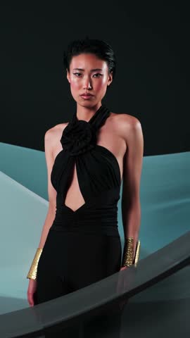 Vertical studio portrait of a young asian model in black jumpsuits and bright makeup.