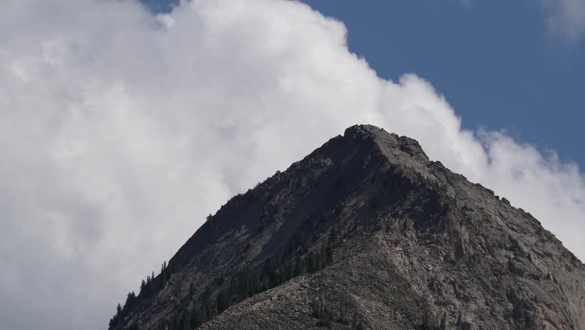 Mountain peak near an alpine lake with clouds passing by near Kebler Pass, Crested Butte, Colorado on a warm summer day with bright blue skies.