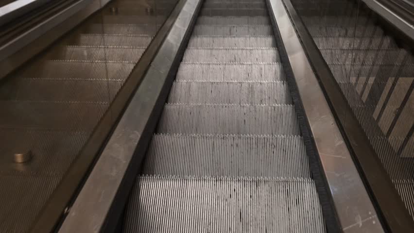 Descending escalator shown from perspective of rider, including arrival at the bottom