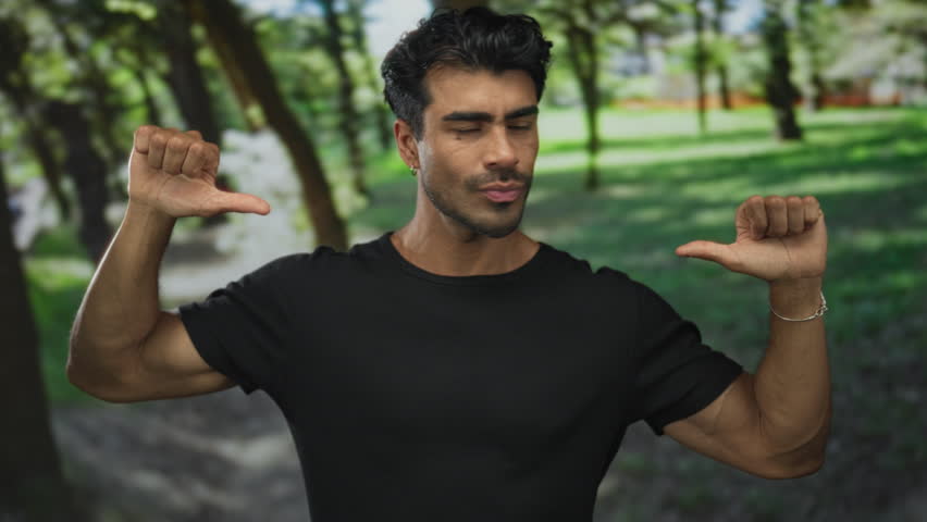 Young hispanic man pointing thumb to chest in sunny green park outdoors, gesturing self reference; confidence.