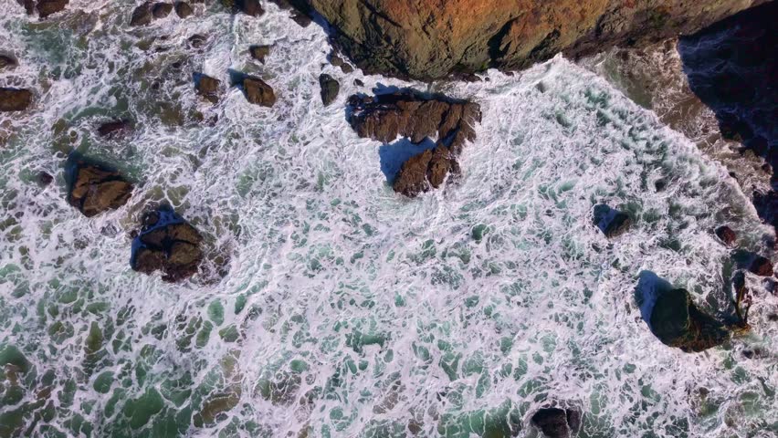 Turquoise waters meet the shore, framed by dramatic coastal cliffs and crashing waves along the rugged and beautiful California coastline