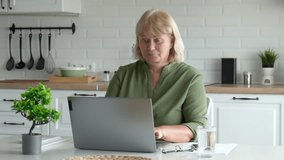 Female at home with devices. Lady with blonde hair participating in virtual conference from kitchen. Adult woman concentrating on digital meeting on laptop while sitting at kitchen counter with plants - Powered by Shutterstock - Get 15% off with code: PIKWIZARD15