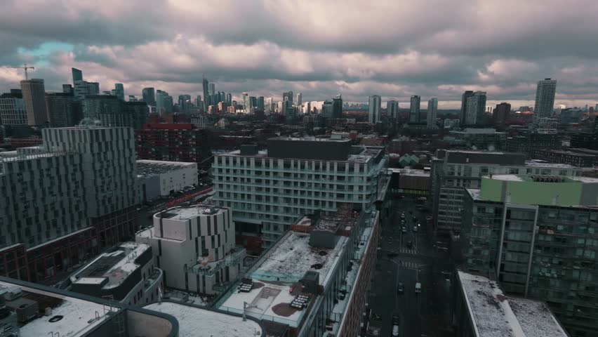 Sunset aerial of Toronto’s Distillery District with the Gardiner Expressway and a TTC streetcar at the Distillery Loop. Golden-hour light reveals a rich blend of heritage brick and modern urban motion
