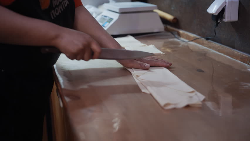 A professional chef precisely divides rolled-out dough into perfectly even squares for making traditional dumplings in a restaurant kitchen.