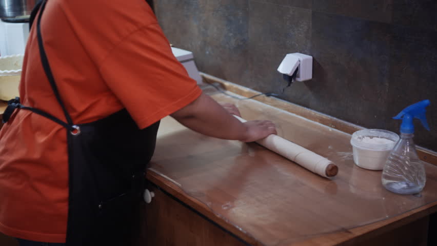 A chef expertly rolls out fresh dough with a traditional rolling pin to prepare manti dumplings at a busy food court. Showcasing authentic culinary techniques and food preparation.