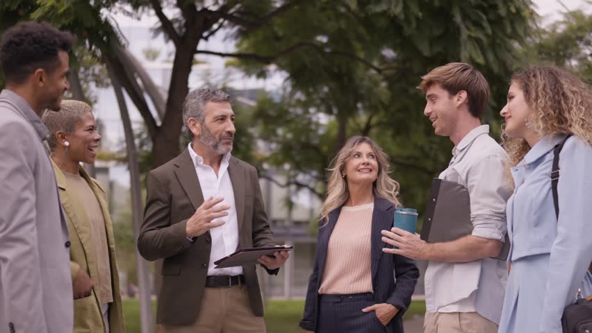 Business professionals engaging in an outdoor meeting at a city park. A senior manager with a tablet leads the discussion with his team