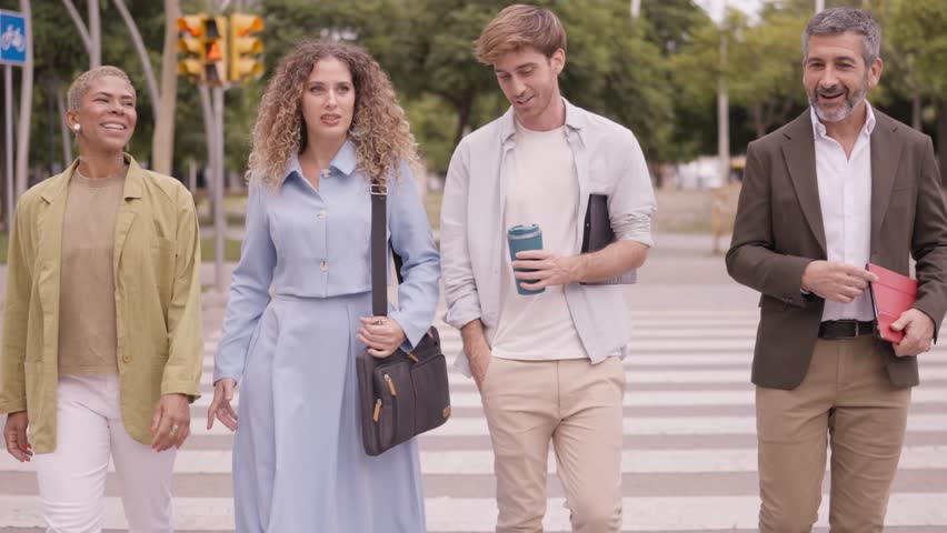 Group of four multiethnic colleagues talking and laughing together while crossing the street. Professional coworkers walking to the office