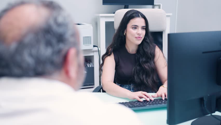 Female receptionist in a dental clinic speaking with a patient while typing on the keyboard. Professional healthcare worker providing assistance