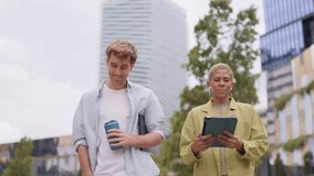 Cheerful young male and female coworkers talking and walking through a modern business district. They are holding a tablet and a coffee cup - Powered by Shutterstock - Get 15% off with code: PIKWIZARD15