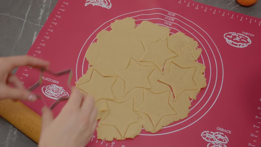 A woman and her young boy enjoy making homemade cookies. They roll out dough and use cookie cutters to create fun star shapes together in their kitchen.