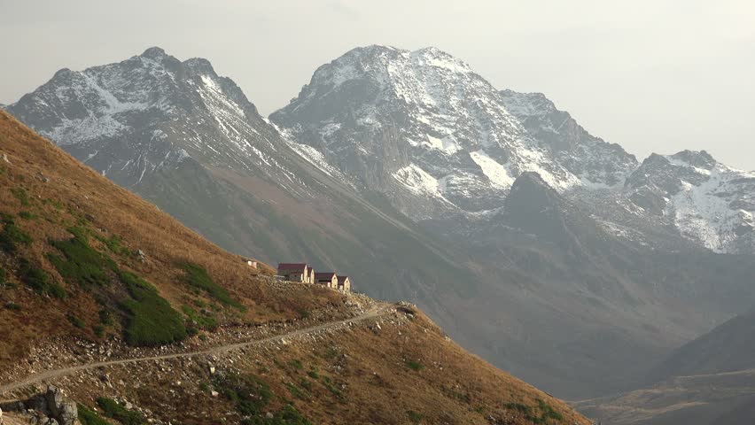 Autumn view of chalets on a treeless slope surrounding snowy mountain peaks. Highland mountain homes overlook rugged terrain as nature and landscape define the alpine background.