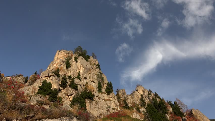 Time lapse clouds over rocky mountain slope with sparse trees in Atlas Mountains. Shifting clouds sweep across rugged Atlas terrain shaped by semi arid and steppe climate patterns.