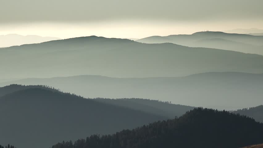 Panoramic view of afternoon light on successive forest covered ridges of the Pyrenees Mountains. Soft haze drifts through layered hills as muted sunlight shapes the expansive Pyrenees landscape.