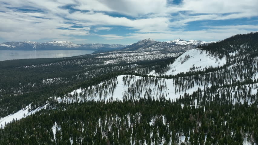 Aerial view rotating over snowy mountains of Tahoe, cloudy, winter day in USA
